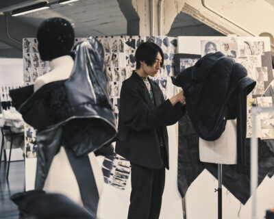 student adjusting garment on a dress form with fashion drawings on two bulletin boards behind him
