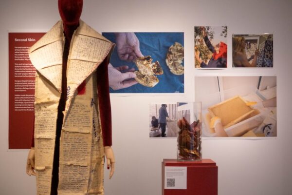 A coat made of paper on a mannequin with photos of natural materials behind it