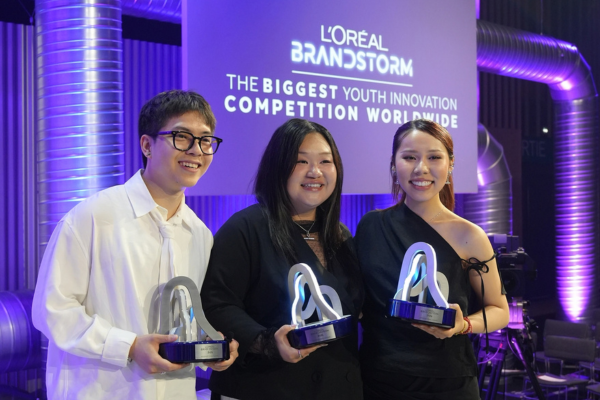 three smiling students stand holding their trophies on a purple lit stage