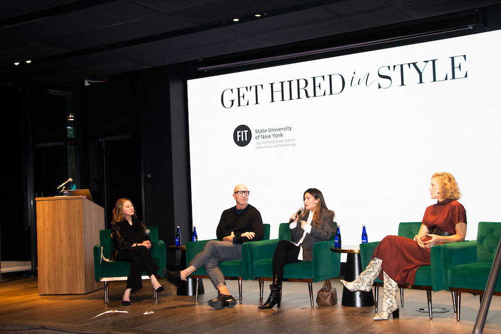 four panelists sitting on chairs on stage with screen behind them