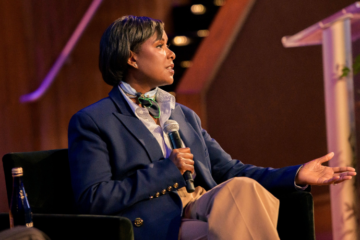 Felita Harris seated, holding a microphone, onstage at a recent event