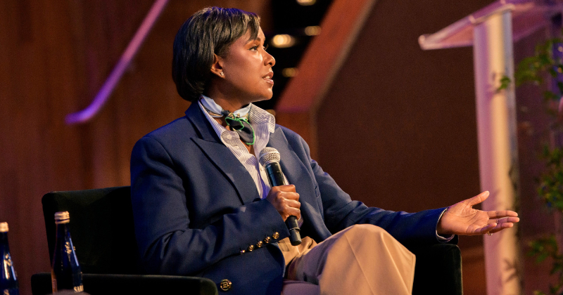 Felita Harris seated, holding a microphone, onstage at a recent event